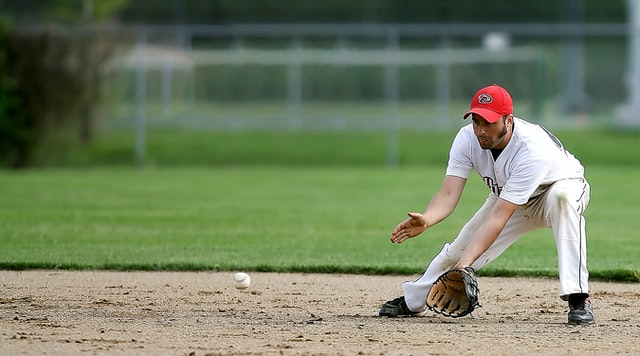 A man about to catch a baseball that is heading toward him close to the ground