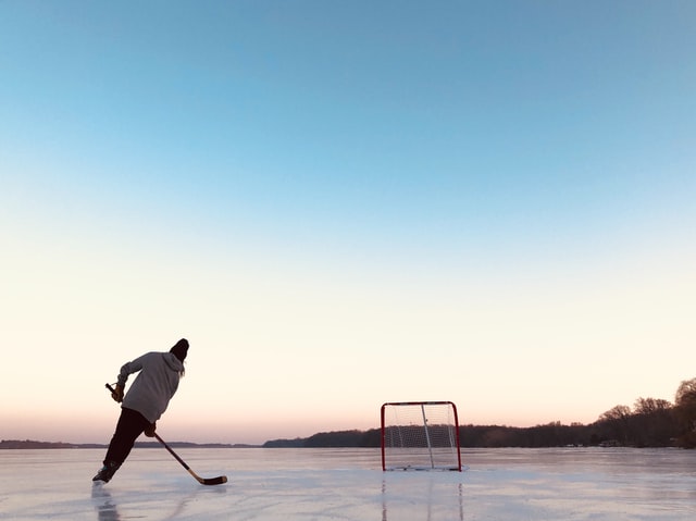 A person holding a hockey stick  skates toward a hockey goal across a frozen pond or lake